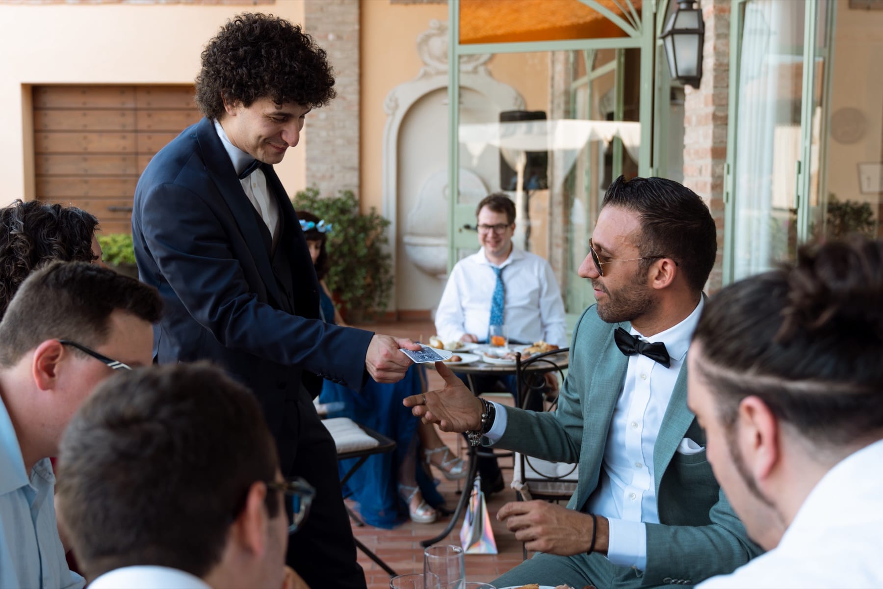 Matteo Angrisano consegna una carta da gioco a un ospite durante un ricevimento all'aperto